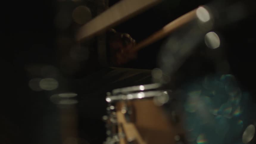Sweaty man energetically drumming on a drum set on a dark stage
