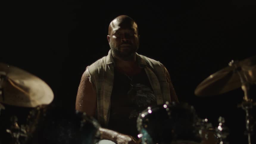 A man glistening with sweat and looking tired sitting at his drum set