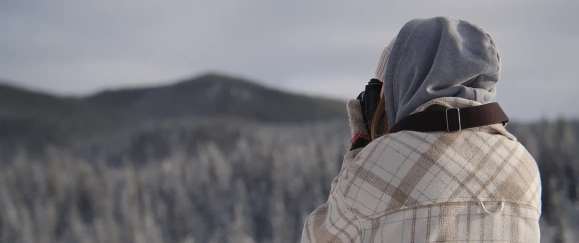 A woman holding a camera taking a photograph of snow covered trees