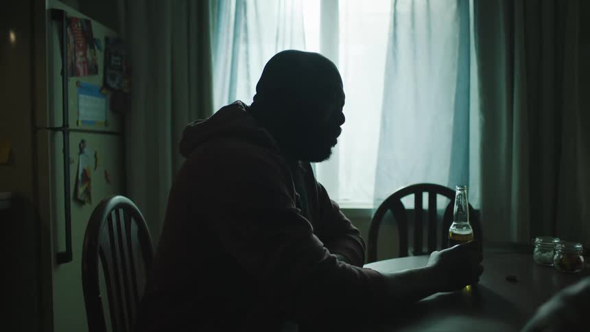 A man is sitting at a table with a beer when a boy brings a drawing to him