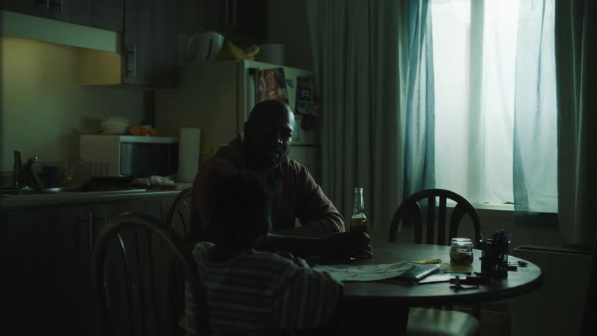A man is sitting at a table with a beer as he talks to his young son