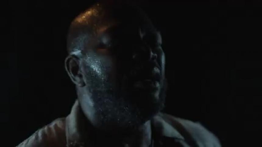 A black man is in a dark room and a strobe light is flashing on his face
