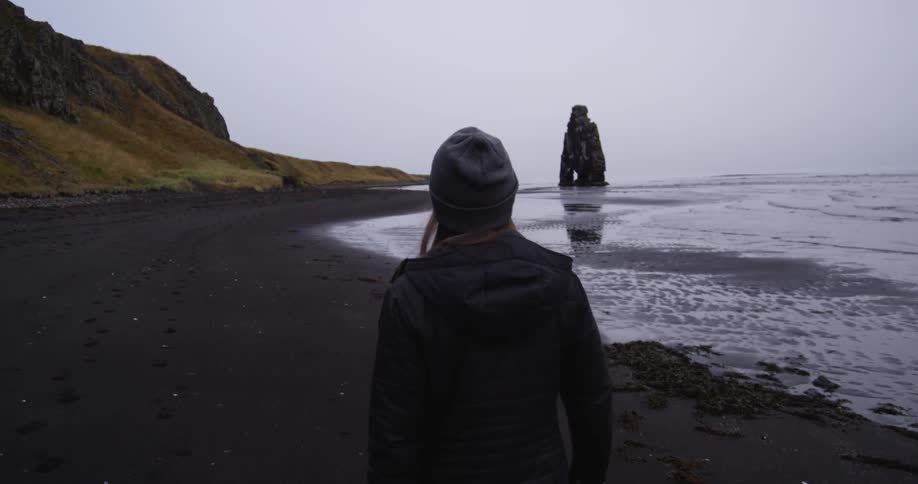 A woman is walking along the shore on a cloudy day