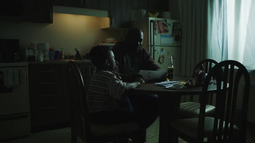 Father and son sitting on the dinning table inside the dimly lit kitchen at home