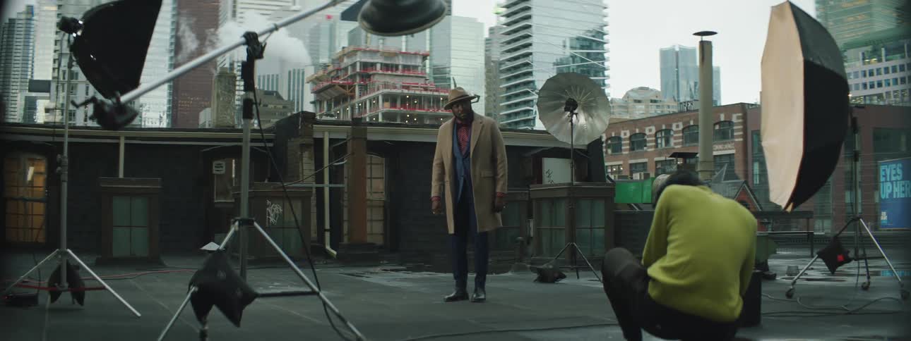 Man wearing a hat and coat on the roof of a building in the city modeling for a photographer