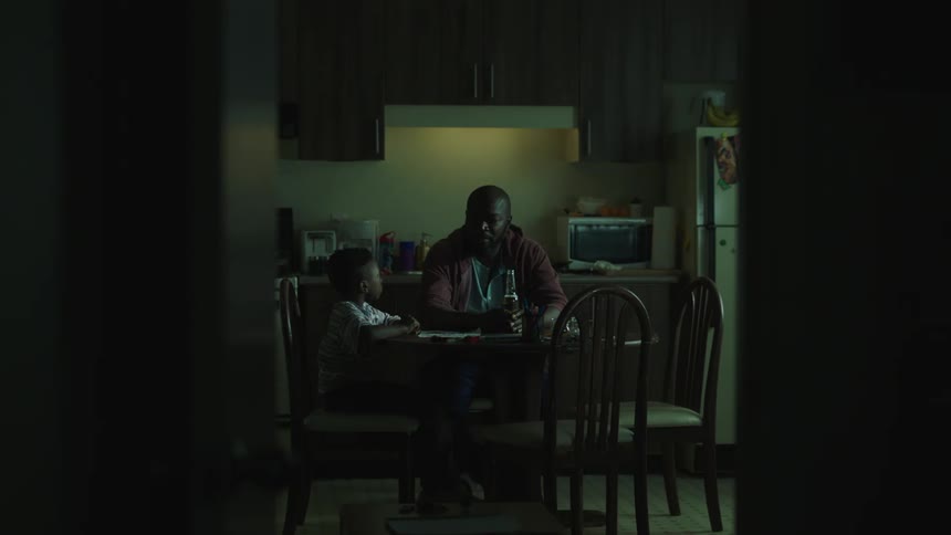 A man and a boy are sitting at a kitchen table then the boy gets up and leaves