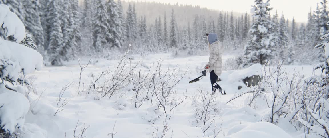 Young woman walks on the snow in the forest carrying a camera at morning