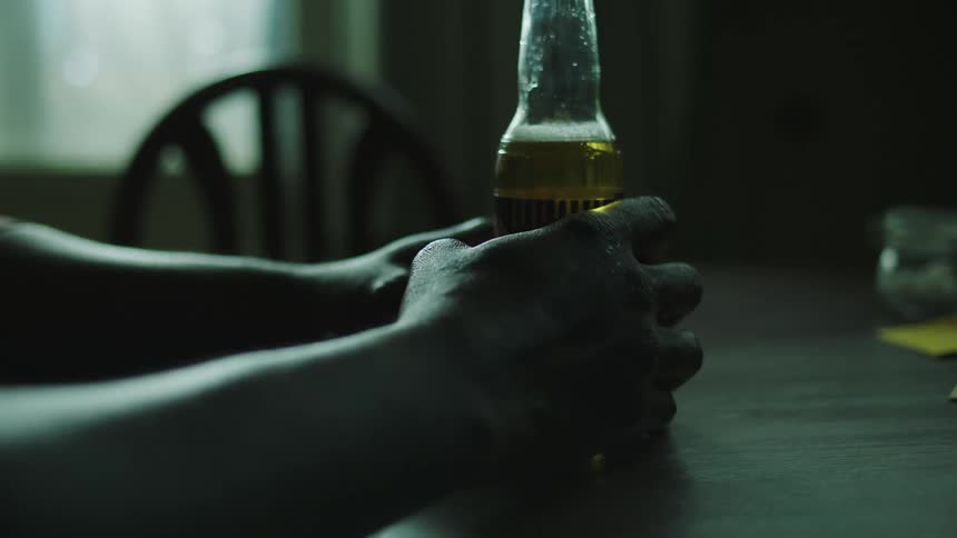 Man sitting at a table holding a beer receives a map from another person