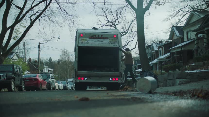 A garbage man collects a bag and throws it in the truck