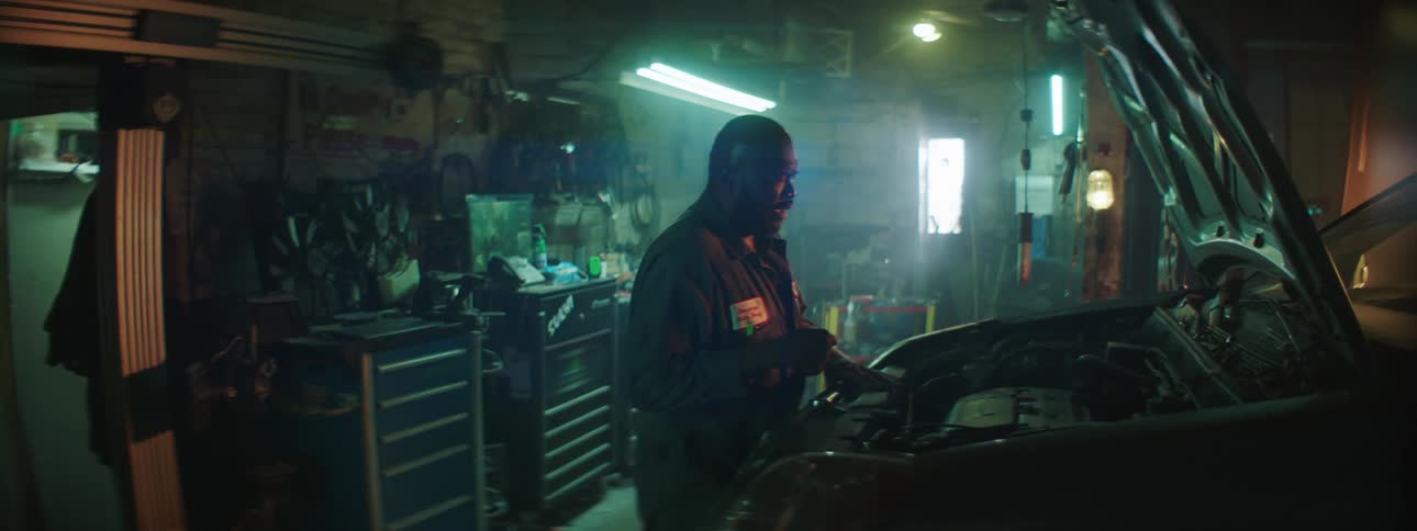 Man strains with wrench on engine then stands painting before covering his face in aggravation