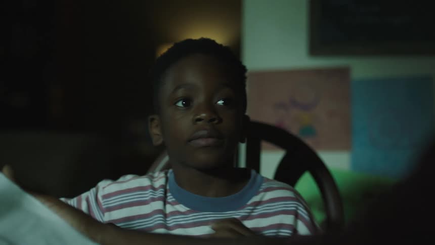 A boy carrying a piece of paper happily sits down at the table and shares his artwork