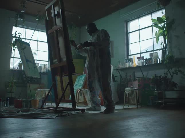 Artist works in artist studio using large brush before flicking paint off it