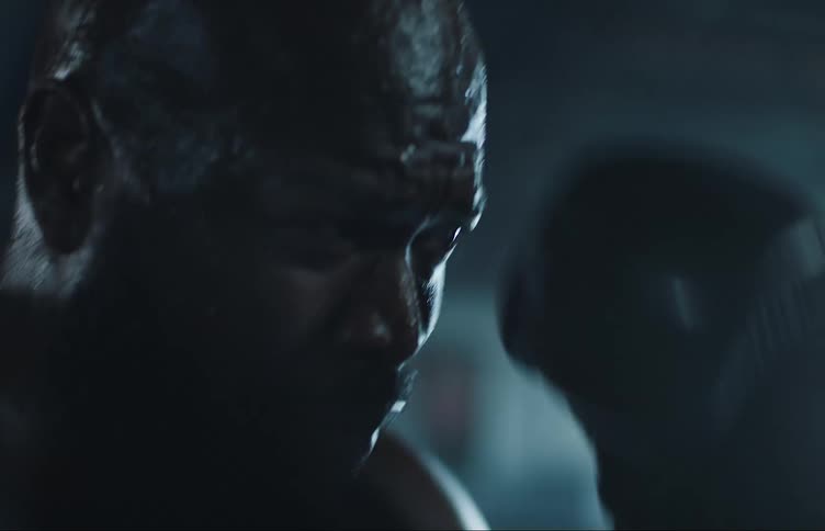 A sweating man throws punchings in a dimly lit boxing gym
