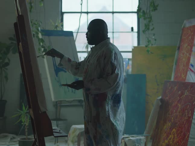 A man is painting on a canvas filled with artwork