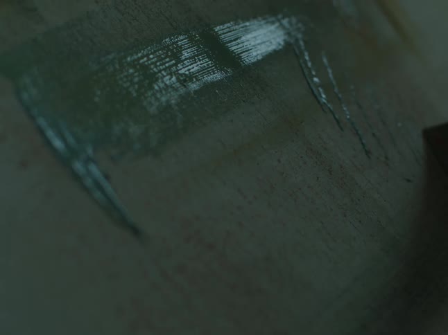 Brush applies paint lightly on a canvas inside a dimly lit room