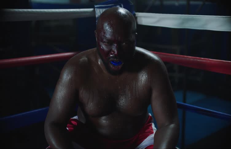 Boxer covered in sweat and blood sits in corner of ring panting
