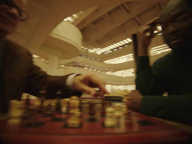 Two men are sitting at a table in a library and playing chess