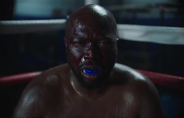 A boxer is sitting down in a boxing ring and is sweating