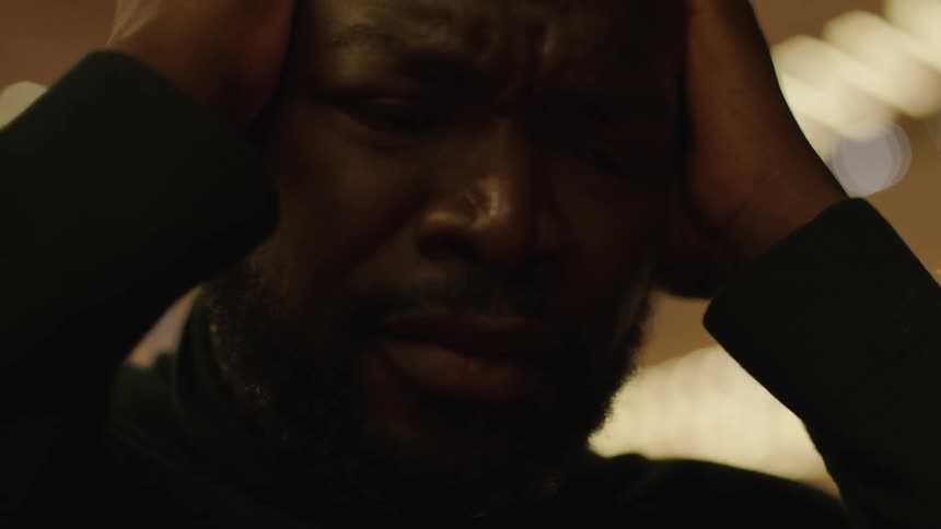 Sad depressed man holding his head on his hands under strobing lights