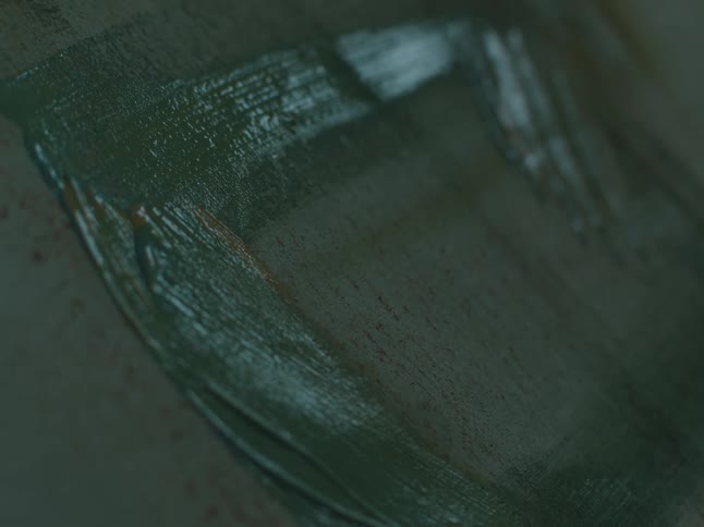 Close up of a brush spreading paint lightly over a canvas inside a dimly lit room