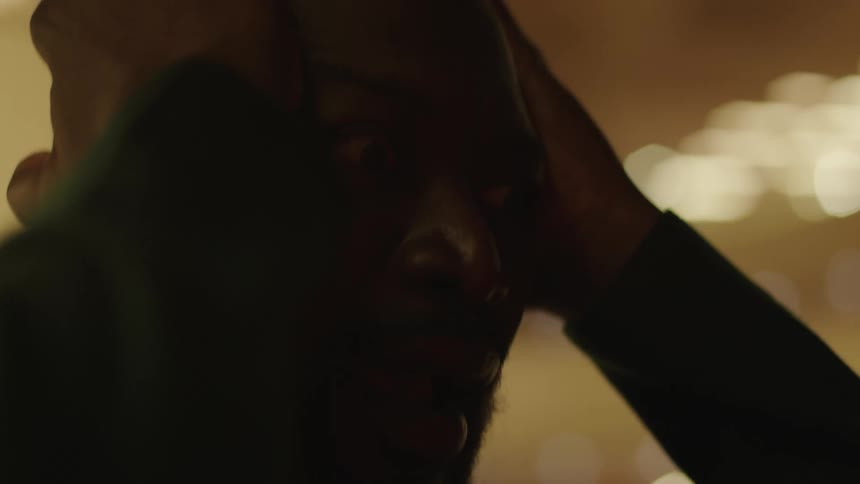 A black man with bulging eyes is holding his head as a strobe light flashes on his face