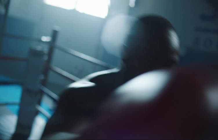 Strong muscular man boxing to the camera over a ring inside a dimly lit gym