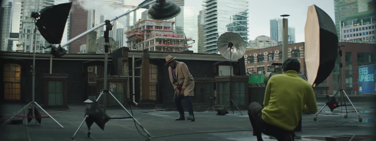 A male model turns and poses for a photographer taking pictures on a city building rooftop