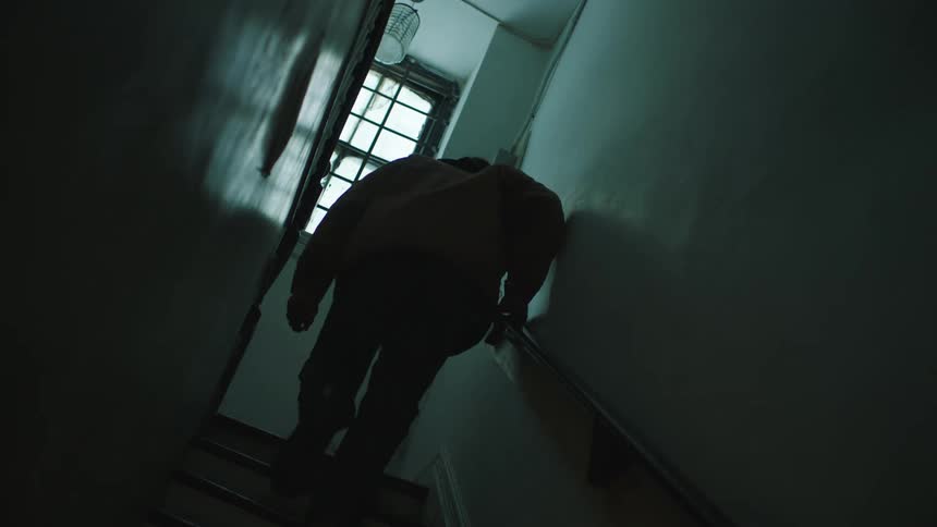 Silhouette of a man walking up a dimly lit staircase at home