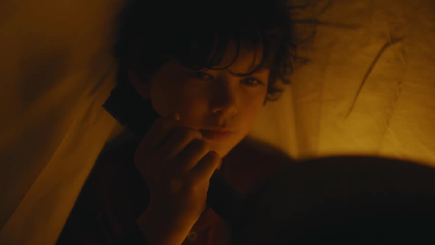 A child is using a flashlight in the blanket tent