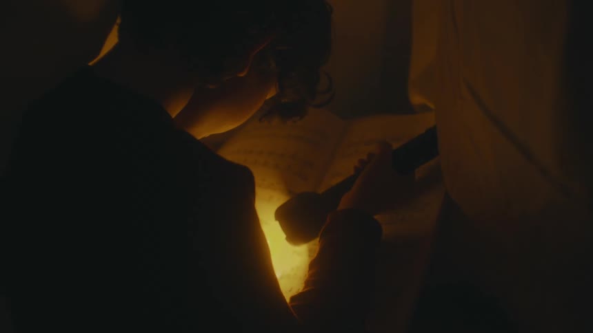 Young boy reading a book with a flashlight inside a dark room at home