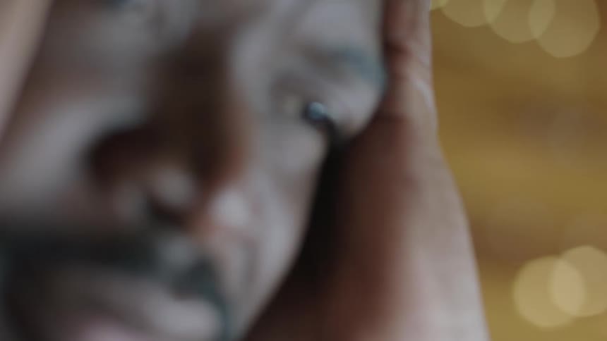 Out of focus footage of a nervous man holding his head on his hands under strobing lights