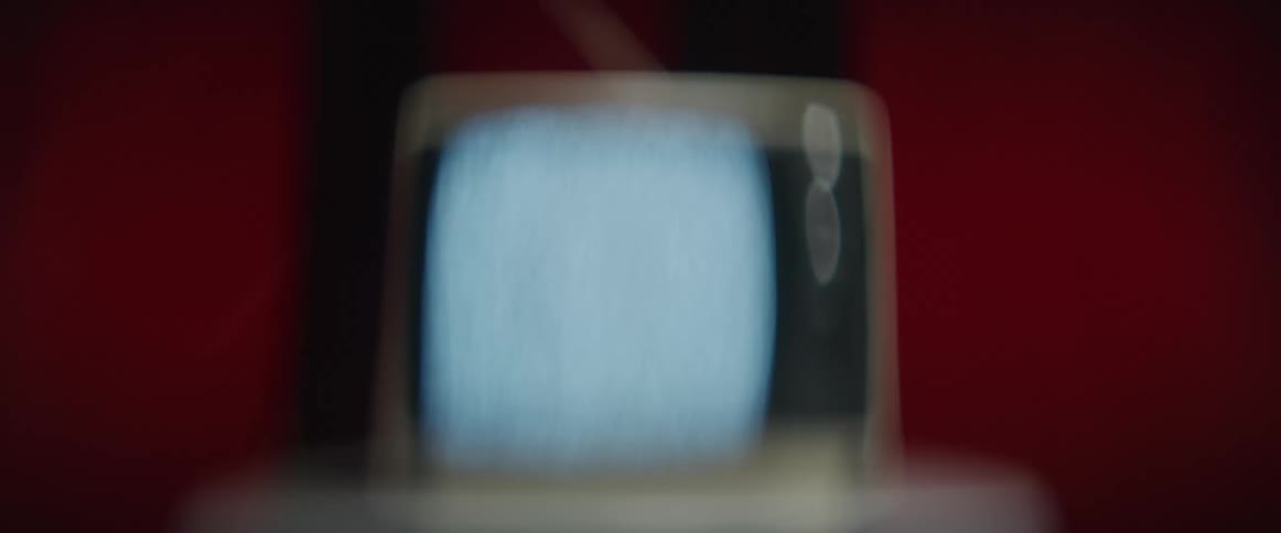 Distorted footage of a vintage television set showing static in front of a red wall