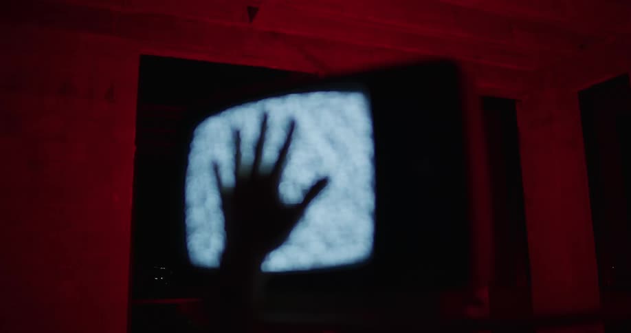 The silhouette of a hand reaching up on a static television screen then sliding back off