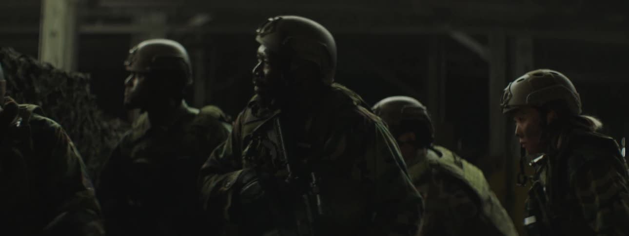 A soldier lobs a grenade over a wall and the rest of the troop ducks as smoke and dust billow past