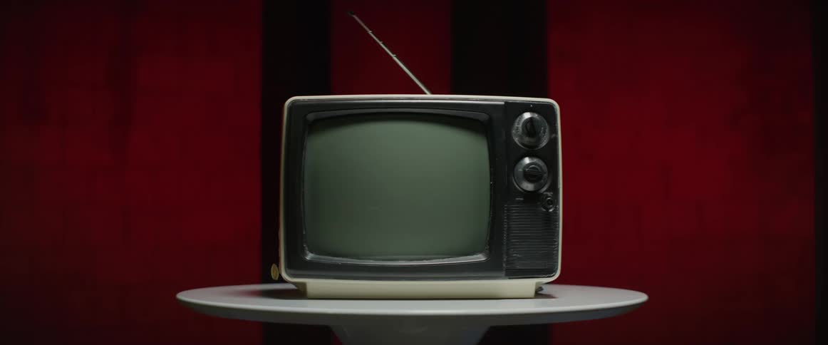 An old model television sits on a round white table with a red wall behind