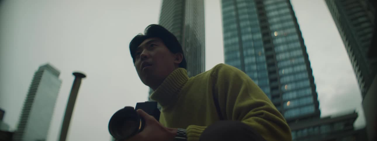 A man adjusts his camera and then waves his subject to move over