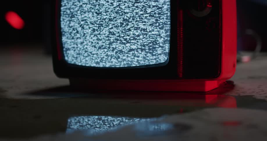Static plays on a television sitting in a puddle of water in a dim room with concrete floors