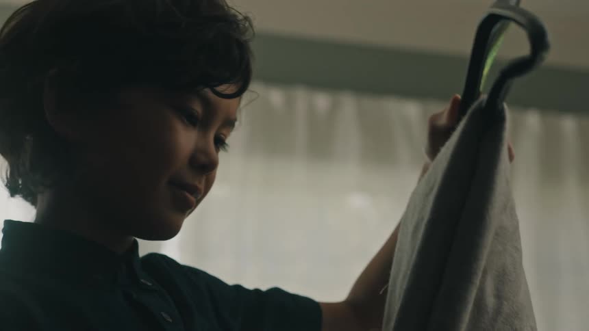 Young man standing inside a room at home picks up a hanger with a towel