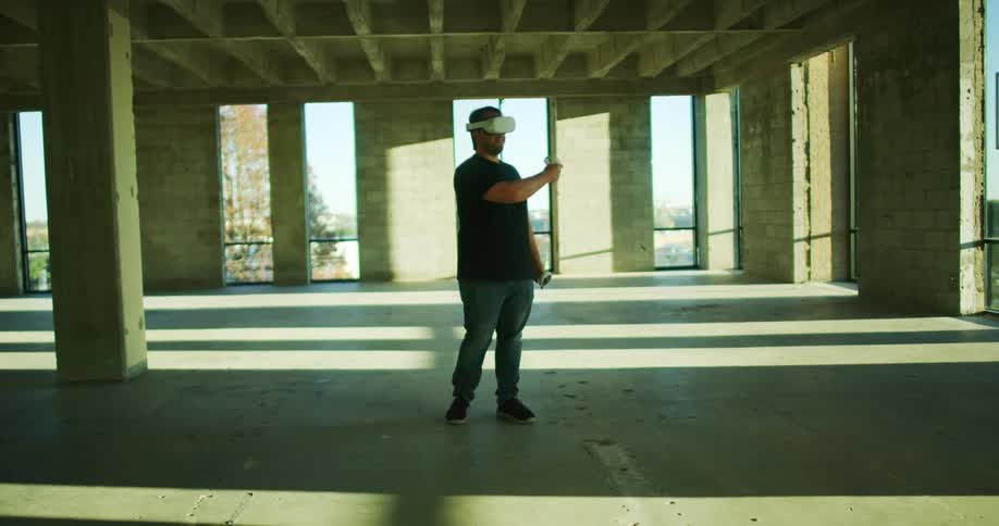 A man stands in an empty parking level wearing vr glasses and using hand controllers
