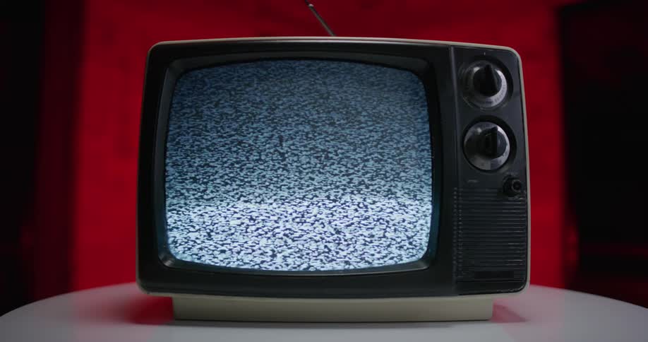 A television set with dials and an antenna sits on a small round table playing static