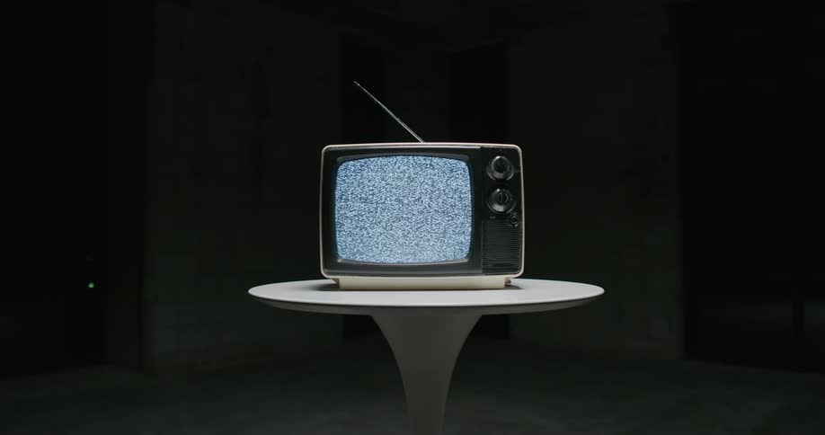An old television is sitting on a table in a dark room and turning off and on