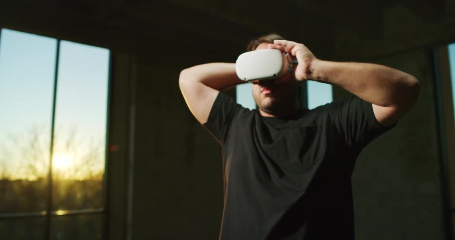 Man standing inside a room at sunset puts on a virtual reality vr set