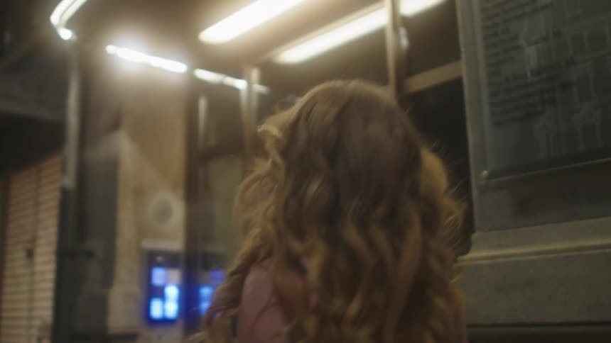 Woman wearing evening wear walks along street at night passing closed storefronts