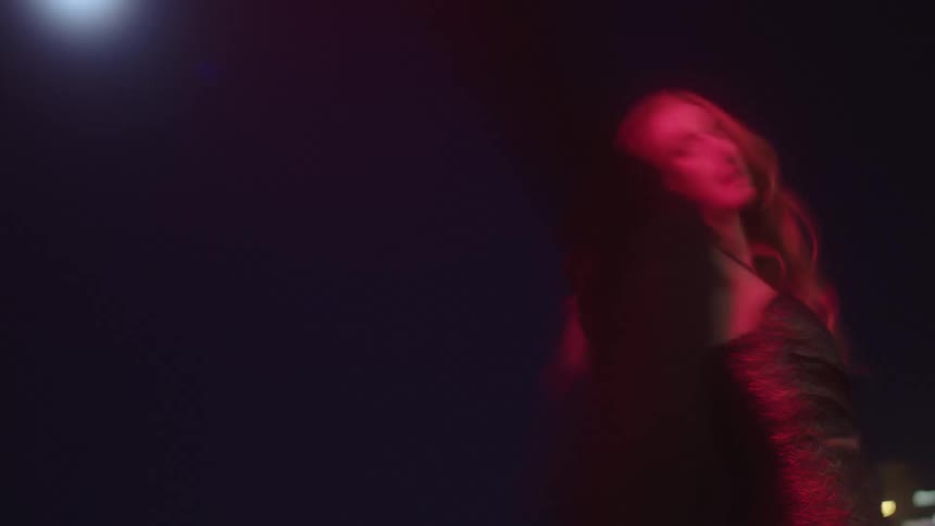 Speed up footage of a young woman walking around the streets under a red light at night