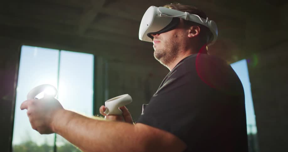 A man wearing a virtual reality headset is holding gaming controllers as he plays a game