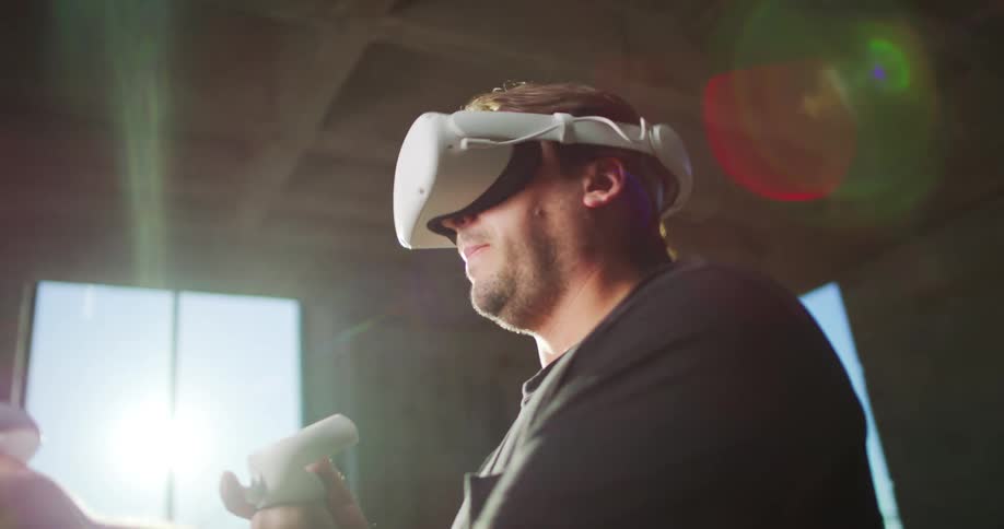 Man with black t shirt and equipped with a vr headset and motion controllers uses virtual reality indoors