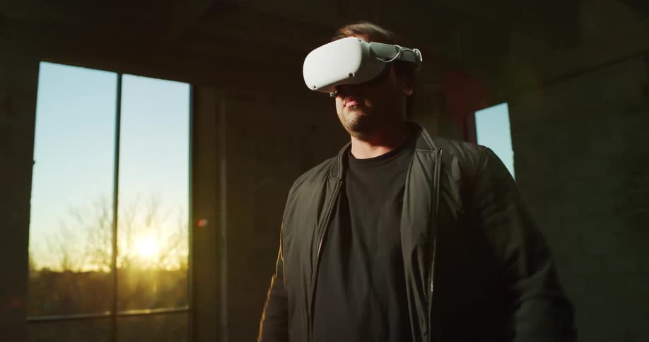 A man is standing near a window and putting on virtual reality gear