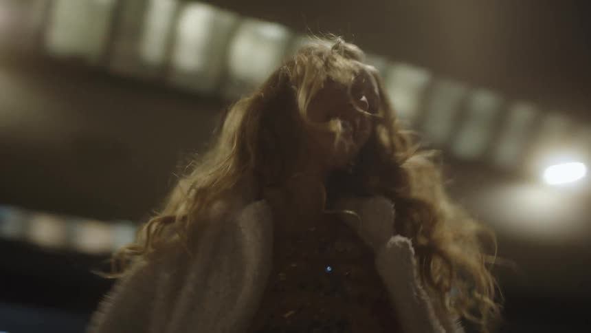 Young blonde woman wearing a shiny dress dances while walking on the city streets at night