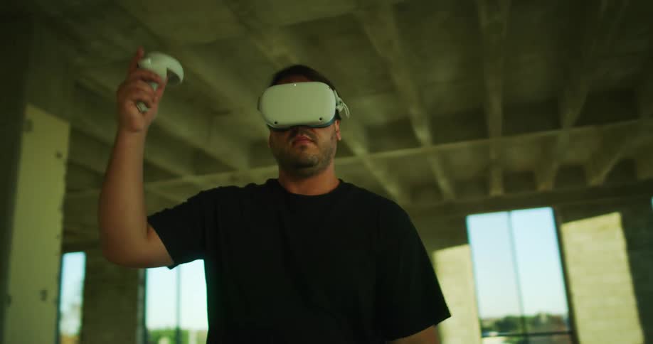 A man is standing in an empty warehouse and playing a virtual reality game