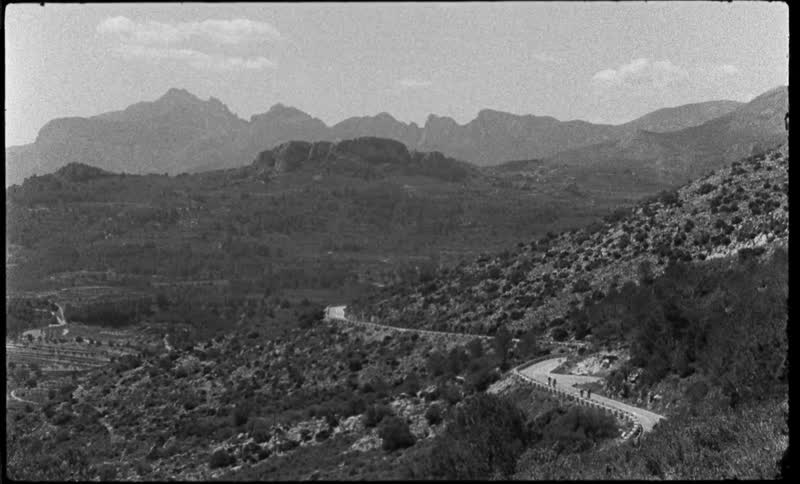 Black and white footage of a cyclists riding on a road through the desert caught on vintage film